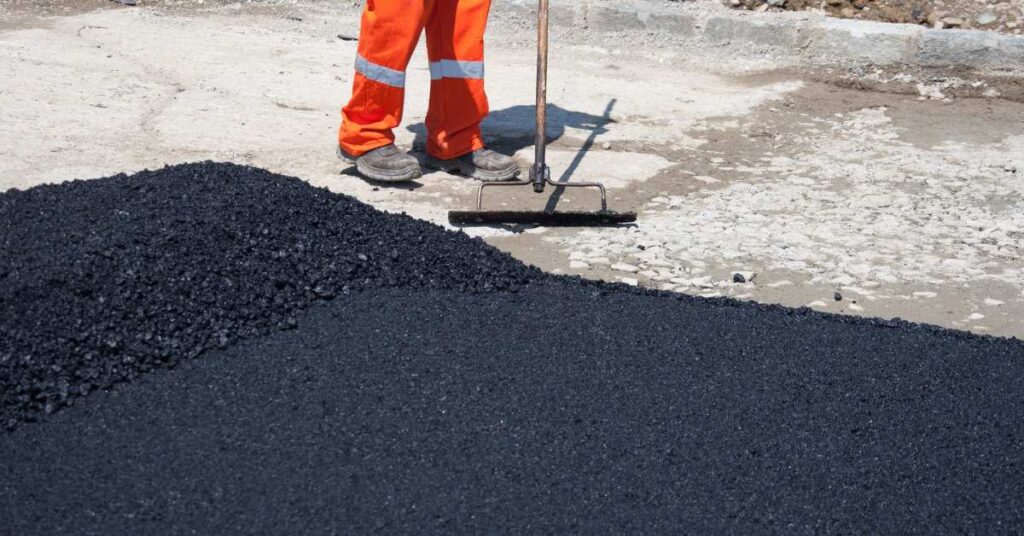 Worker preparing asphalt paving surface by leveling fresh asphalt on the site.