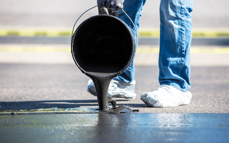 a person pouring a black liquid into a puddle of water